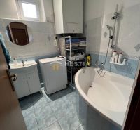 A compact bathroom in a 3-room apartment with a bathtub, sink, washing machine, and storage space.