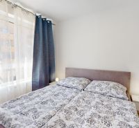 Bright bedroom in a two-room apartment with patterned bedding and nightstands.