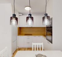 A kitchen in a 2-room apartment with white furniture and a floor with a wood decor.