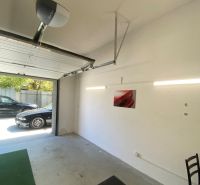 A garage with open doors, a car outside, a bright interior, a picture on the wall.
