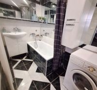 A bathroom with black and white tiles, a sink, a bathtub, and a washing machine in a studio apartment.