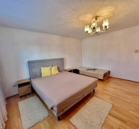 A bedroom with two beds, a wooden decor floor, a bright chandelier, a carpet.