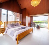 Bedroom in a villa with large windows, wooden elements, and a bed with linen.