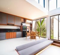 A villa with a wooden decor floor, kitchen, and dining area. Large windows provide a view of the garden.