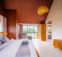 Interior of a villa with a large bed, wooden decor, and a large window.