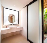 A bathroom in a villa with a sink, a round mirror, and sliding doors.
