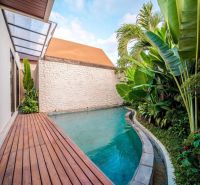 A villa in Bali with a pool surrounded by greenery and a floor with a wooden decor.