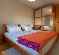 Bedroom in a 4-room apartment with a bed, mirrored wardrobe, and wooden decor flooring.