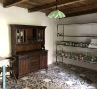 Interior of a family house with a wooden ceiling and patterned tiles, a cabinet, and shelves with glasses.