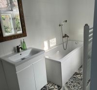 A bathroom in a family house with a white bathtub, sink, and decorated mirror.