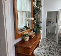 Wooden dresser with flowers and a mirror, designed tiles on the floor.