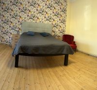 Bedroom with a bed, floral wallpaper, wood-patterned flooring, and a tiled stove.