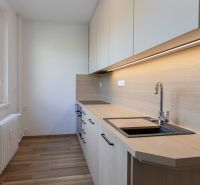 The kitchen in a 3-room apartment with a wooden decor floor and light cabinets.