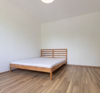 A bedroom with a bed, a floor with a wooden decor, in a three-room apartment.
