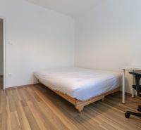 A bedroom in a 3-room apartment with a bed, a desk, and a floor with a wooden decor.