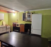 A kitchen in a cottage with a wooden decor floor, simple furniture, and appliances.