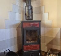 A stove in the corner of a cabin with a wooden decor floor and tiled cladding.