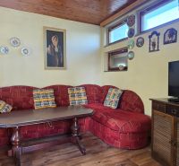 Living room of the cottage with a red sofa, wooden furniture, and a floor with a wooden design.