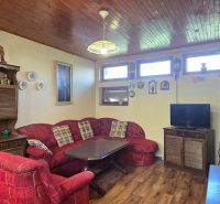 Living room of the cottage with a red sofa, wooden furniture, and a floor with a wooden decor.