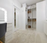 A wardrobe in a family house with white cabinets and a lighted mirror.
