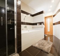 A bathroom in a family house with a bathtub, a shower corner, and tiles with a wooden decor.