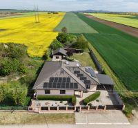 A family house on Močenská Street in Cabaj-Čápor, surrounded by a field of yellow rapeseed flowers.