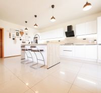 A kitchen in a family house with white cabinets, a bar counter, and tiles.