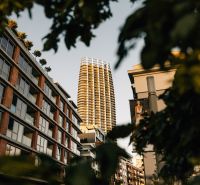 A high-rise building in the background of a street with greenery and residential units in Bratislava.