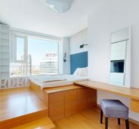 Bright bedroom with a tall window, a desk, and a wood-patterned floor.