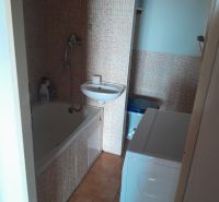 A bathroom in a studio apartment with a bathtub, sink, washing machine, and mosaic tiles.