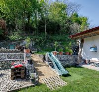 A family house in Potzneusiedl with a courtyard, slide, and stone walls surrounded by greenery.