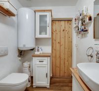 A bathroom in a family house with a toilet, sink, and cabinets, with a wooden decor floor.