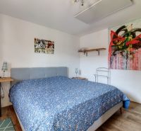 Bedroom in a family house with a bed, wooden decor flooring, and an art painting.