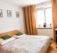 A bedroom in a 2-room apartment with a bed, a desk, and a wooden-patterned floor.