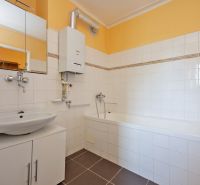 A bathroom in a 2-room apartment with a bathtub, sink, and ochre walls.