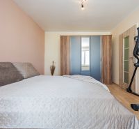 Bedroom in a two-room apartment with a large bed, wardrobe, and exercise bike on a floor with a wooden decor.