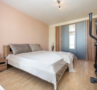 A bedroom in a two-room apartment with a bed, wardrobe, exercise machine, and a floor with a wooden decor.