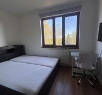 A bedroom with a bed, table, and wooden decor flooring in a three-room apartment.