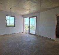A room in a 3-bedroom apartment with a raw concrete floor and white walls.
