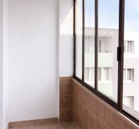 Glazed balcony in a 4-room apartment with light tiles and a view of the apartment building.