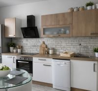 A kitchen in a 4-room apartment with matte white and wooden cabinets and a glass table.