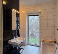 A bathroom with a bathtub and a sink in a family house, white and black tiles, a window with a view.