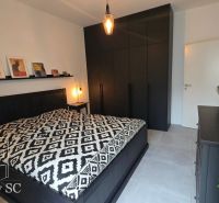 A bedroom with black furniture, artistic decorations, and a patterned bedspread.
