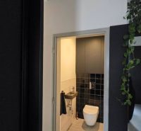 A toilet in a family house with black tiles and a light floor.