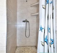 A shower corner with a pebble floor and a curtain with a sea motif in a cottage.