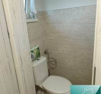 A toilet in a cabin with a wood-patterned floor and beige tiles.