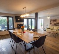Living room with wood-patterned flooring in a family house, furnished with a dining table and a sofa.