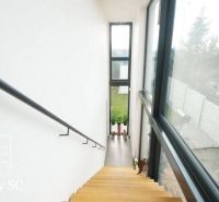 A staircase with a wooden decor in a family house with large windows and a view of the garden.