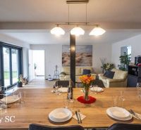 A dining table with glasses and plates in a family house, with a living room in the background.