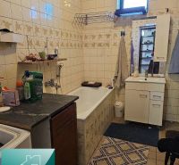 A bathroom in a family house with a bathtub, a sink, and storage cabinets. Tiled walls.